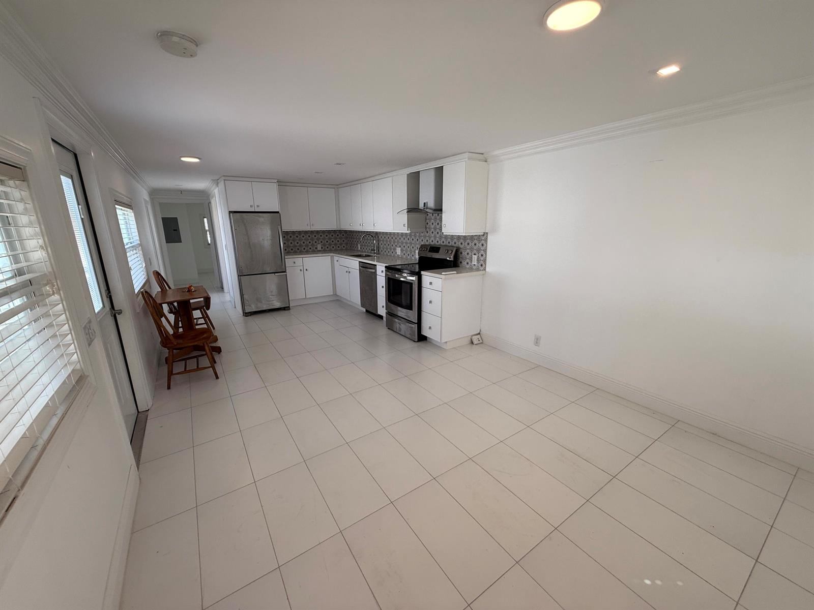 A kitchen features white cabinets, stainless steel appliances, a patterned backsplash, and white tile flooring — 206 Eagle Drive E, Briny Breezes FL 33435, BRINY BREEZES, FL