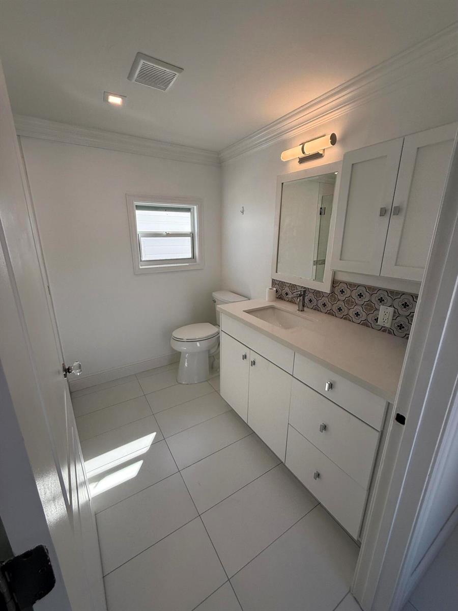 A bathroom features white cabinetry, a light-colored countertop, a patterned backsplash, and white floor tiles — 206 Eagle Drive E, Briny Breezes FL 33435, BRINY BREEZES, FL