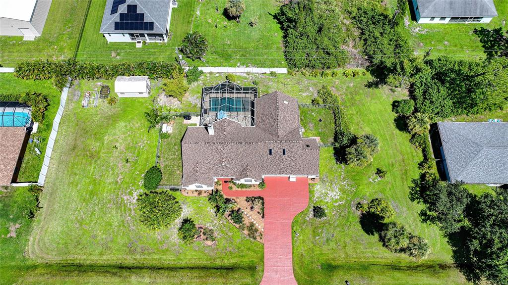 An aerial view shows a house with a red driveway, pool enclosure, and surrounding yard — 5219 GUAVA TERRACE, PORT CHARLOTTE, FL