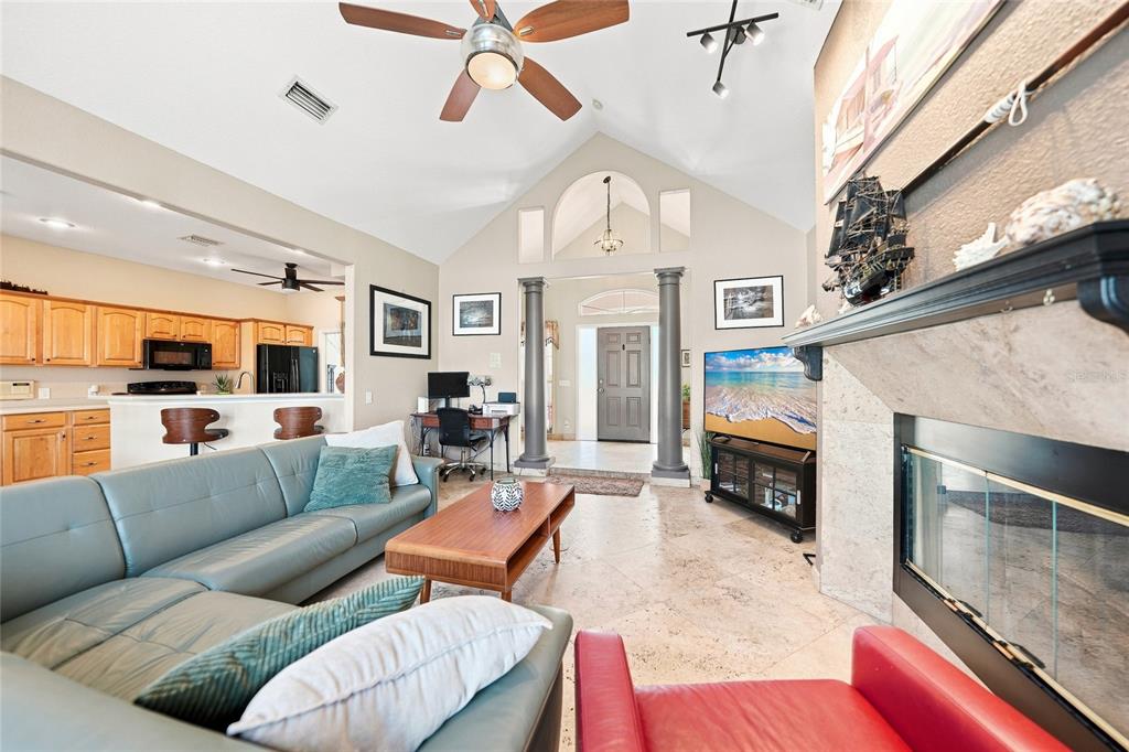 A living room features a vaulted ceiling, stone fireplace, tile flooring, and an open kitchen — 5219 GUAVA TERRACE, PORT CHARLOTTE, FL