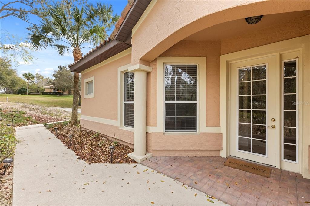 A tan stucco house exterior features a brick entryway, a glass-paneled door, and a walkway — 102 CAMINO REAL BOULEVARD UNIT 102, HOWEY IN THE HILLS, FL