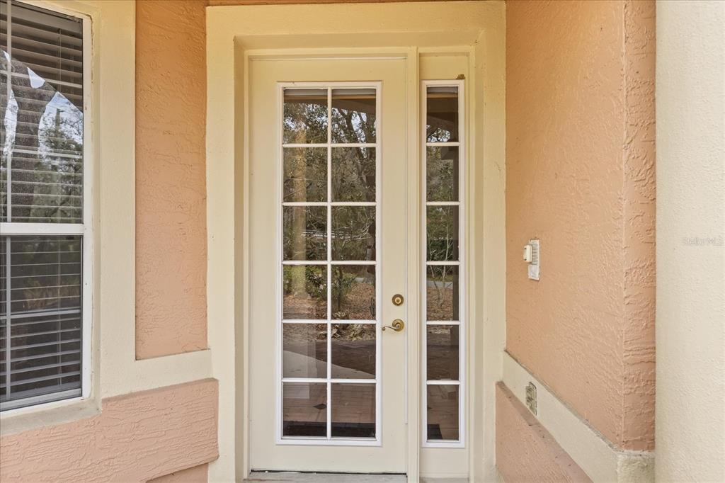 A white French door with glass panes and a matching sidelight on a beige porch — 102 CAMINO REAL BOULEVARD UNIT 102, HOWEY IN THE HILLS, FL