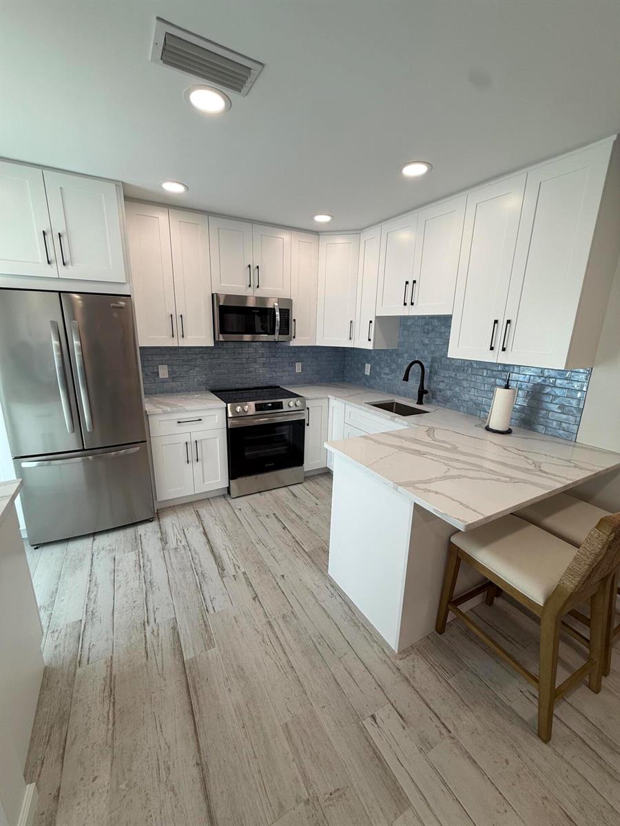 A kitchen features white cabinets, stainless steel appliances, a marble-look countertop, and blue tile backsplash — 370 Wilma Circle # 6, Riviera Beach FL 33404, RIVIERA BEACH, FL