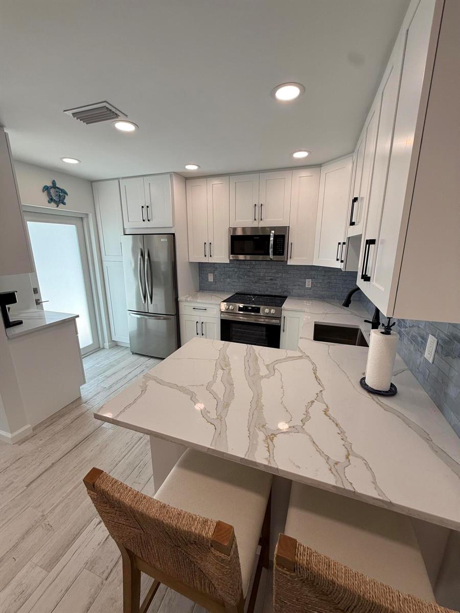 A kitchen features white cabinets, marble-patterned countertops, stainless steel appliances, and a blue tile backsplash — 370 Wilma Circle # 6, Riviera Beach FL 33404, RIVIERA BEACH, FL