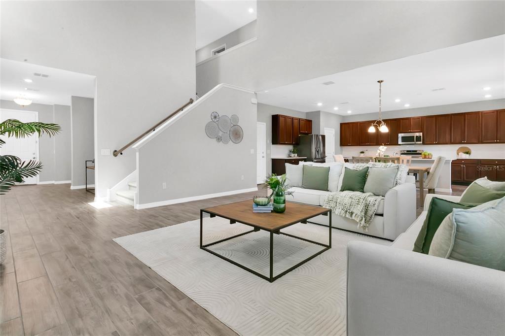 An open-concept living room features light wood-look flooring, a staircase, and an adjacent kitchen — 9169 WAVERLY WALK DRIVE, ORLANDO, FL