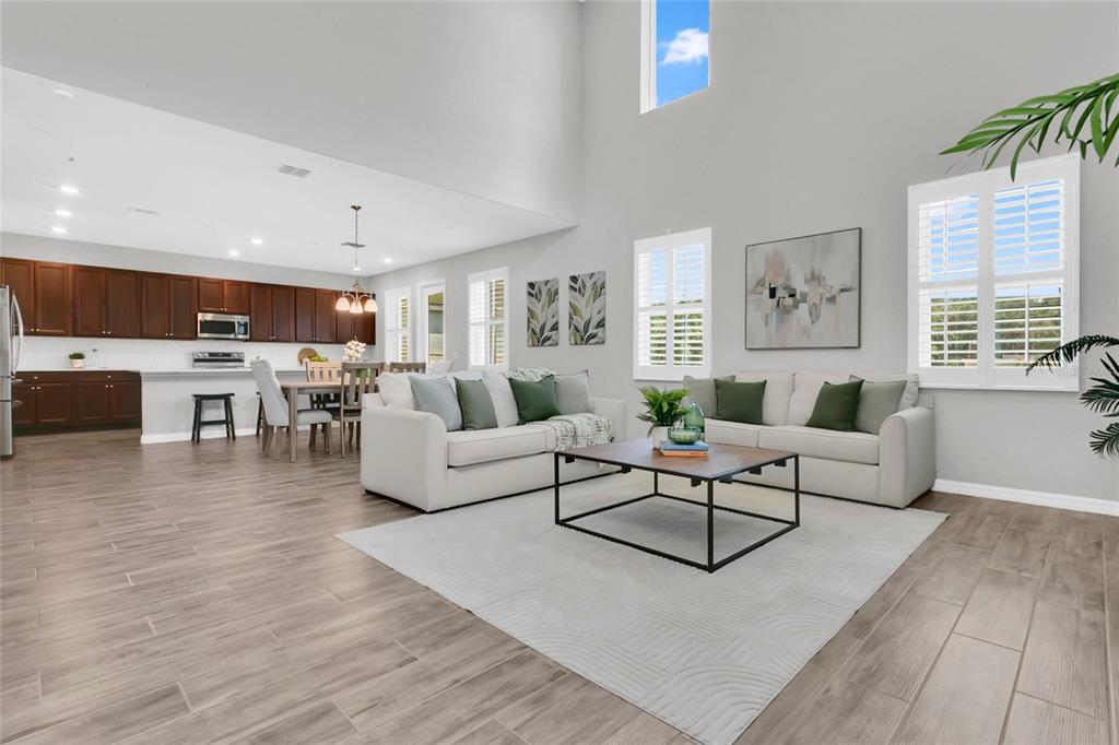 An open-concept living room and kitchen with high ceilings, wood-look tile floors, and neutral furniture — 9169 WAVERLY WALK DRIVE, ORLANDO, FL