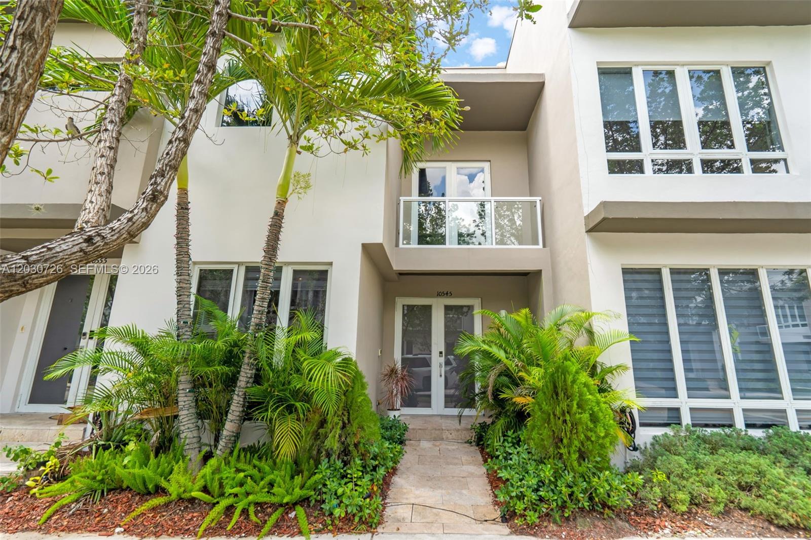 The exterior of a modern two-story townhouse features a glass balcony and lush landscaping — 10545 NW 63rd Ter, Doral FL 33178, DORAL, FL