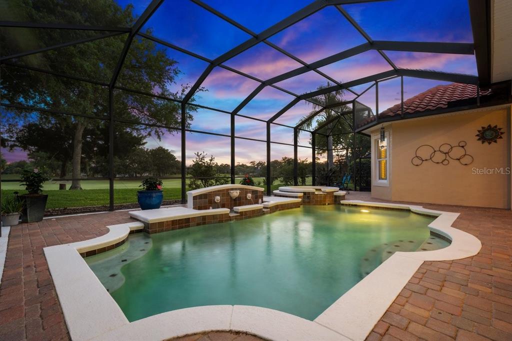 A screened-in pool and spa area with brick pavers overlooking a golf course at sunset — 102 LAGARE STREET, PALM COAST, FL