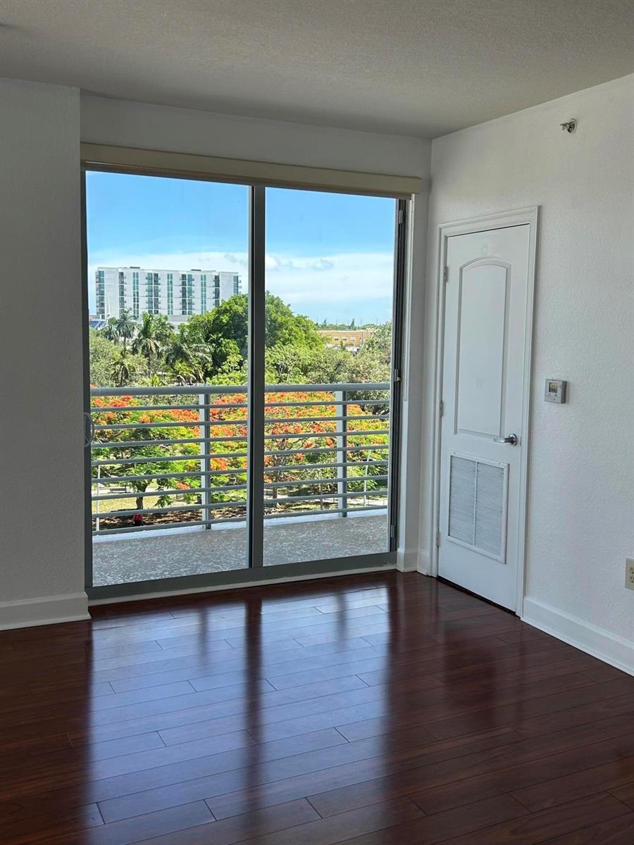 An empty room with dark wood flooring, a sliding glass door to a balcony, and white walls — 1830 Radius Drive # 514, Hollywood FL 33020, HOLLYWOOD, FL