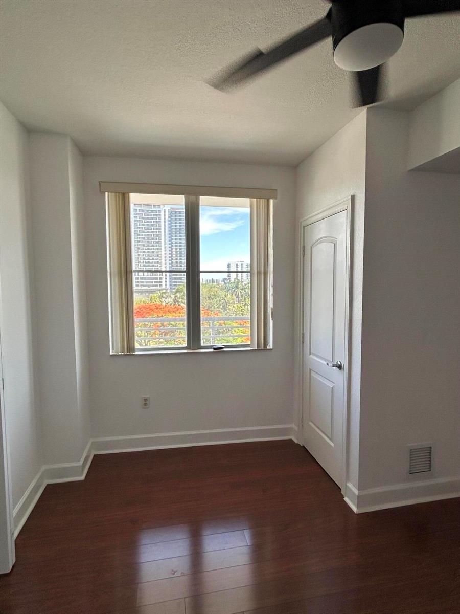 An empty room with wood-look flooring, a ceiling fan, and a window overlooking city buildings — 1830 Radius Drive # 514, Hollywood FL 33020, HOLLYWOOD, FL