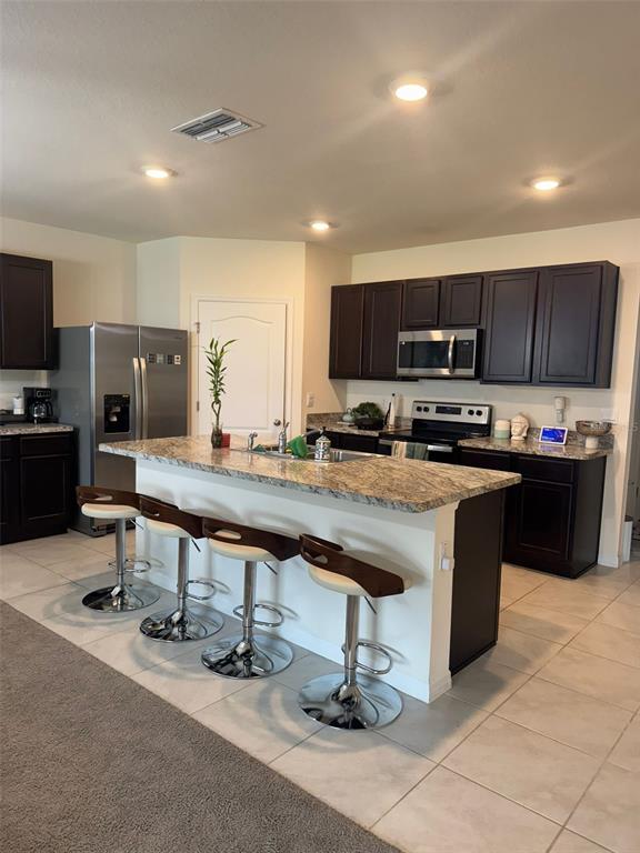 A kitchen features dark wood cabinets, granite countertops, a center island with barstools, and appliances — 823 AUBURN GROVE COURT, AUBURNDALE, FL