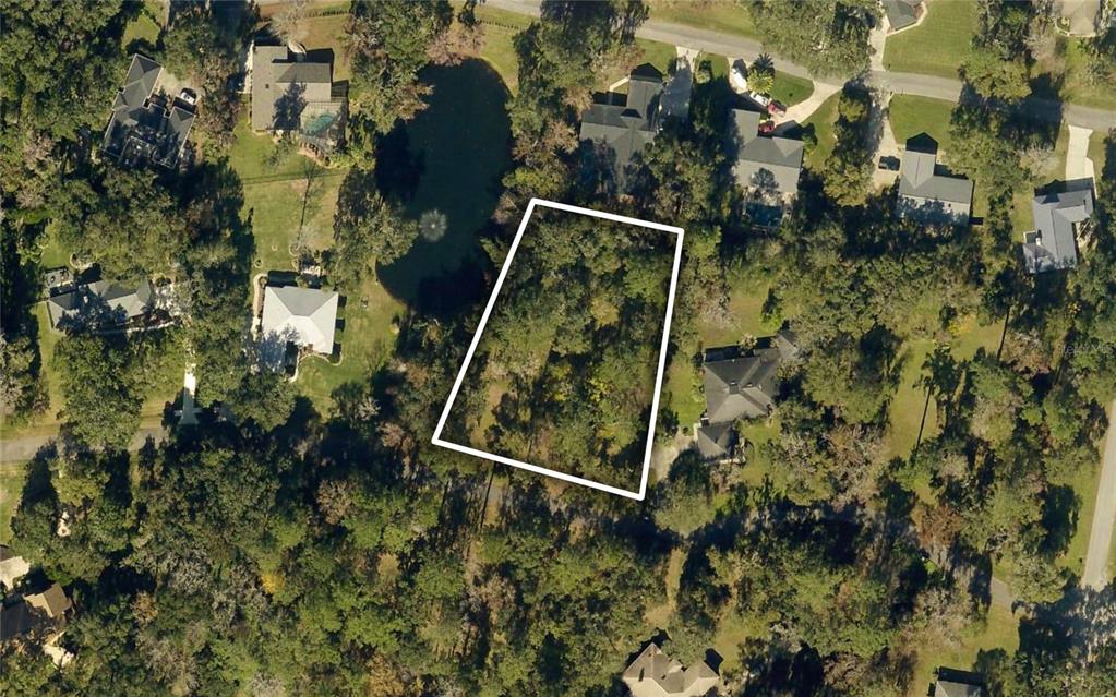 An aerial view shows a vacant, wooded residential lot outlined in white near a pond — TBD NW 46TH STREET, OCALA, FL