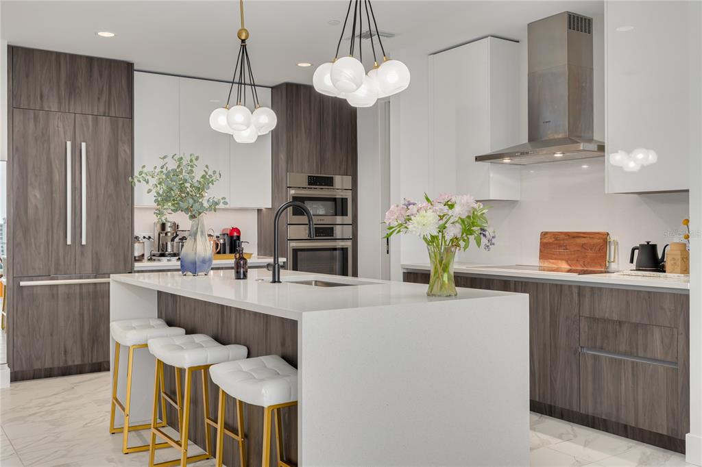 A modern kitchen features a white quartz island, wood-grain cabinetry, and gold-accented bar stools — 777 3RD AVENUE N UNIT 1104, ST PETERSBURG, FL