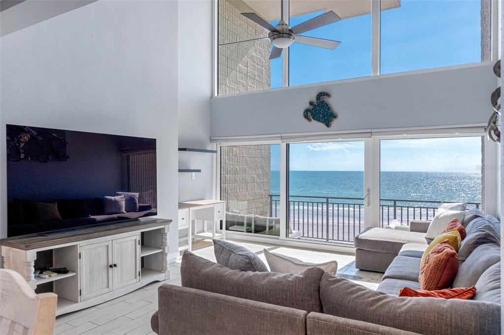 A living room features a large television, a sectional sofa, and floor-to-ceiling windows overlooking the ocean — 19700 GULF BOULEVARD UNIT 403, INDIAN SHORES, FL
