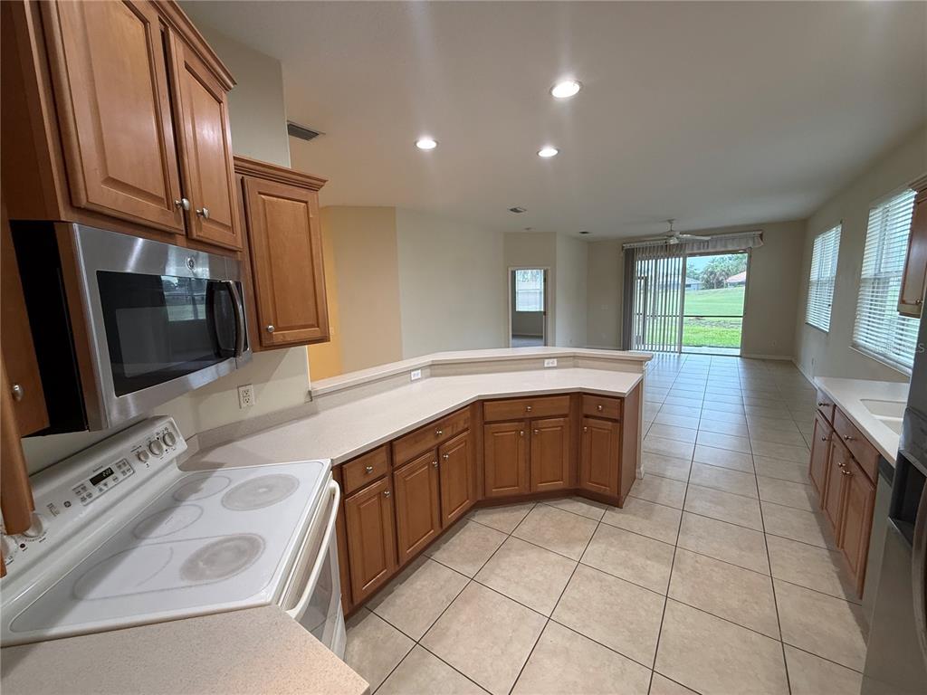 A kitchen with wood cabinets, light countertops, and tile flooring overlooks an open living area — 342 FAIRWAY ISLES LANE, BRADENTON, FL