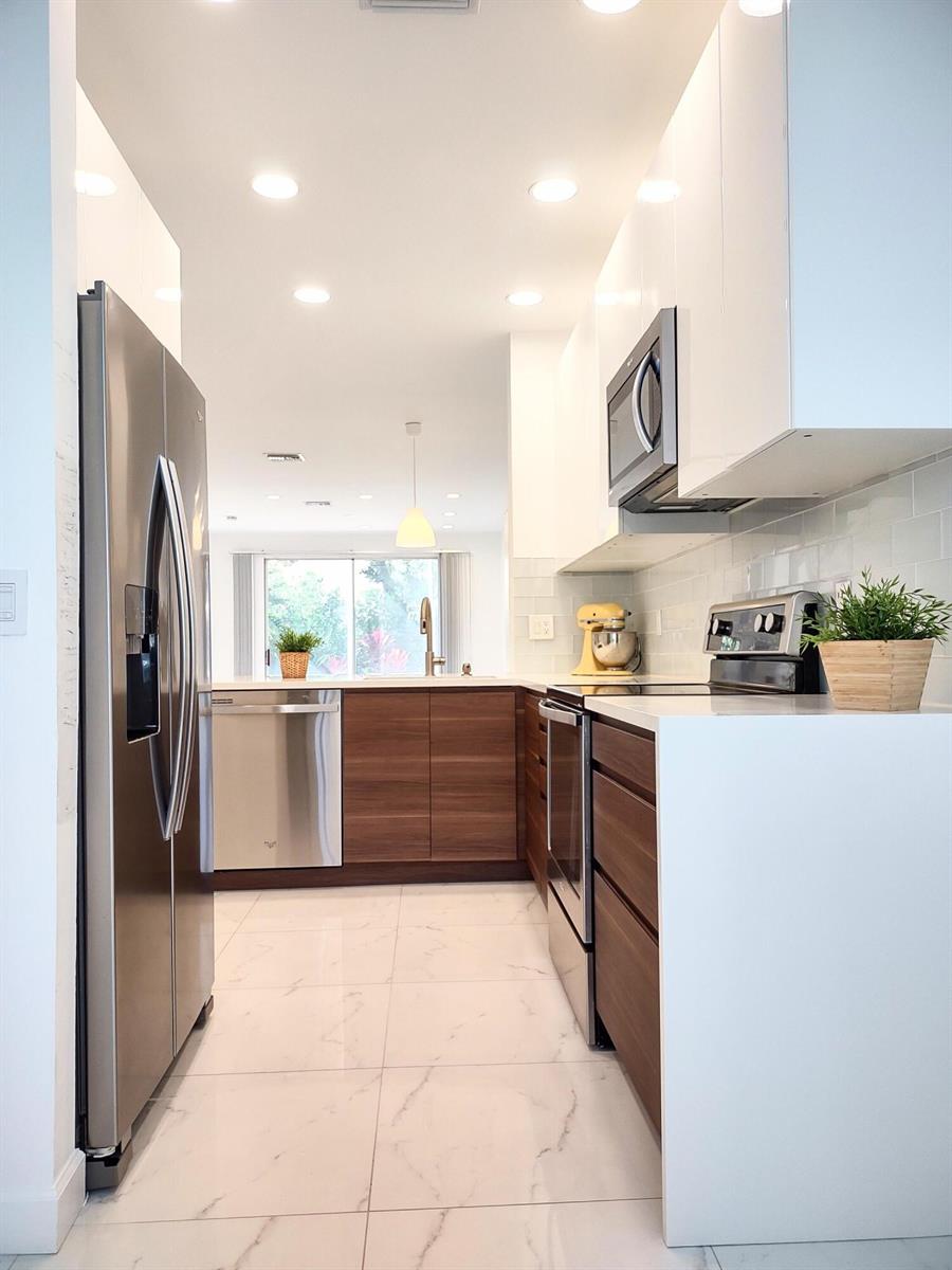 A modern galley kitchen features white upper cabinets, wood-tone lower cabinets, and stainless steel appliances — 6698 Via  Regina, Boca Raton FL 33433, BOCA RATON, FL