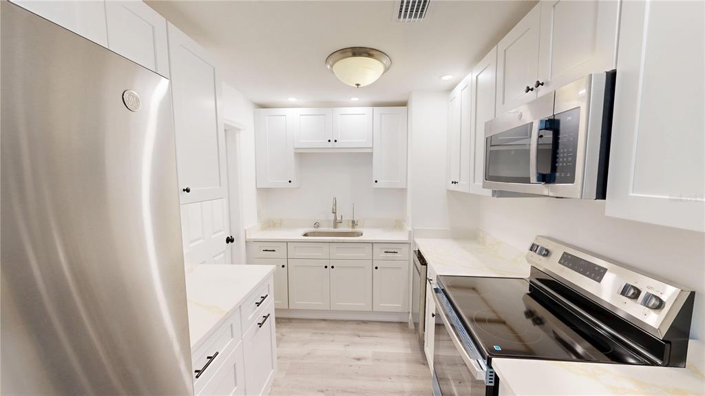 A bright kitchen features white cabinets, stainless steel appliances, and light-colored countertops — 4421 GANDY CIRCLE, TAMPA, FL