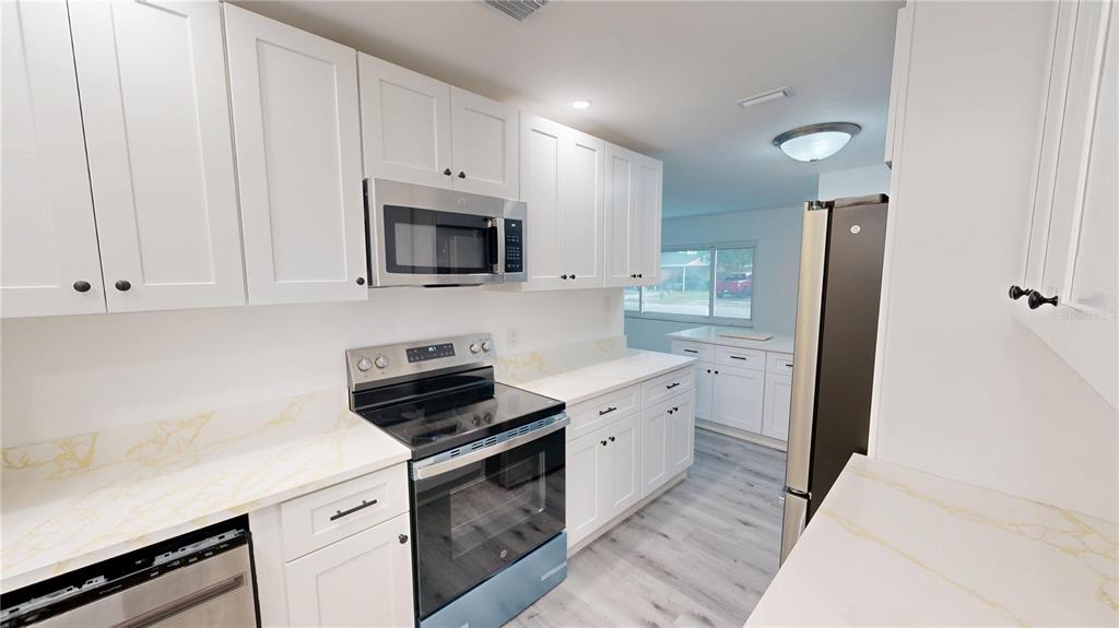 A modern kitchen features white cabinets, stainless steel appliances, and light-colored countertops with gold veining — 4421 GANDY CIRCLE, TAMPA, FL