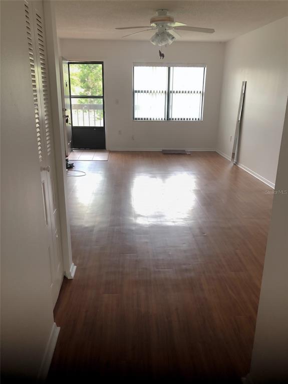 An empty living room features wood-look flooring, a ceiling fan, and a glass-paneled entry door — 305 30TH AVENUE W UNIT A207, BRADENTON, FL