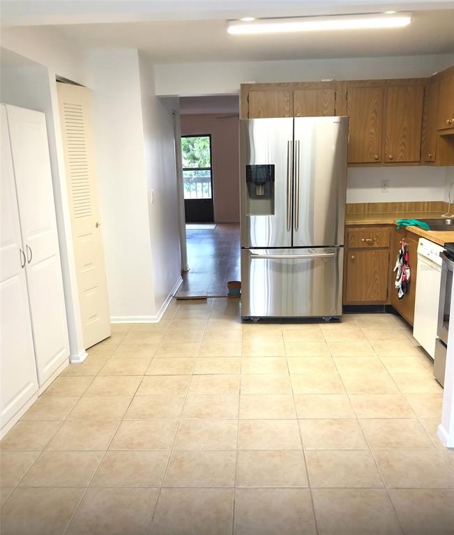 A kitchen features light tile flooring, oak cabinets, and a stainless steel refrigerator — 305 30TH AVENUE W UNIT A207, BRADENTON, FL