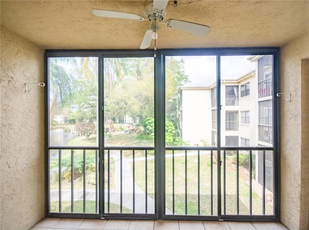 A screened-in balcony with a ceiling fan overlooks a pond and apartment buildings — 305 30TH AVENUE W UNIT A207, BRADENTON, FL