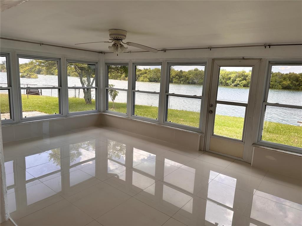 A sunroom with white tile floors, a ceiling fan, and large windows overlooking a lake — 3340 WILSON DRIVE, HOLIDAY, FL