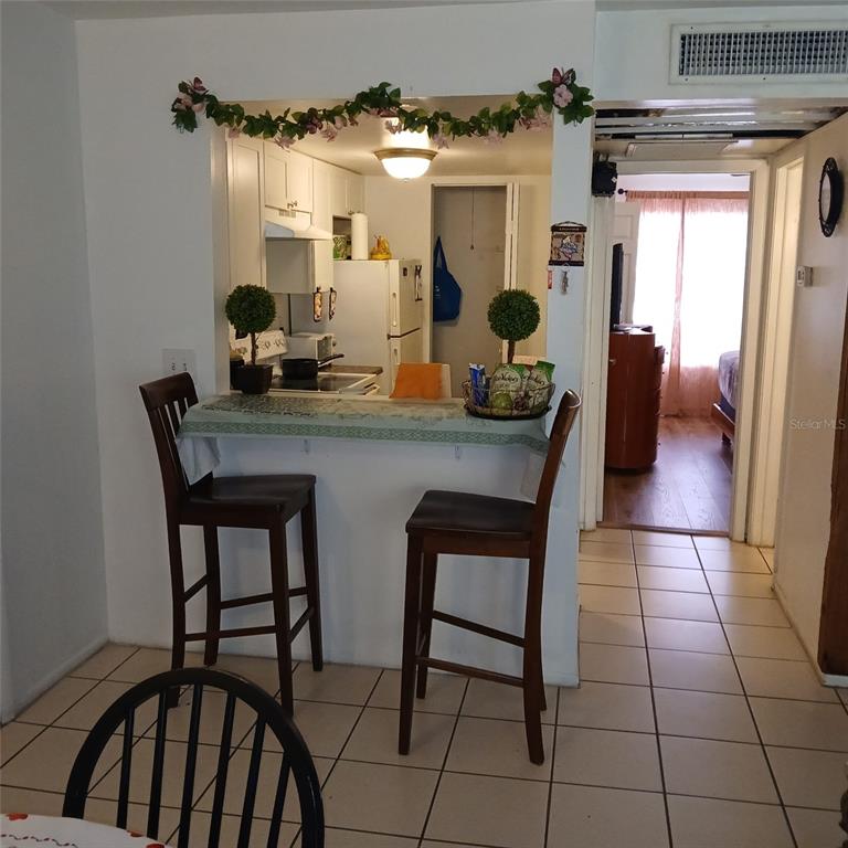 A kitchen with a breakfast bar and two stools overlooks a tiled dining area — 8609 N CHAMPLAIN COURT UNIT 77, TAMPA, FL