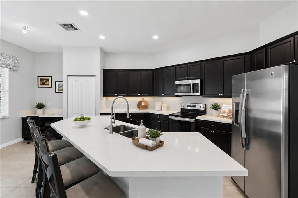 A kitchen features dark cabinets, a large white island with a sink, and stainless appliances — VERO BEACH, FL