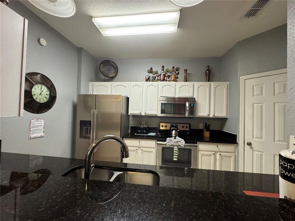 A kitchen features white cabinets, stainless steel appliances, and dark granite countertops — 7664 COMROW STREET UNIT 204, KISSIMMEE, FL