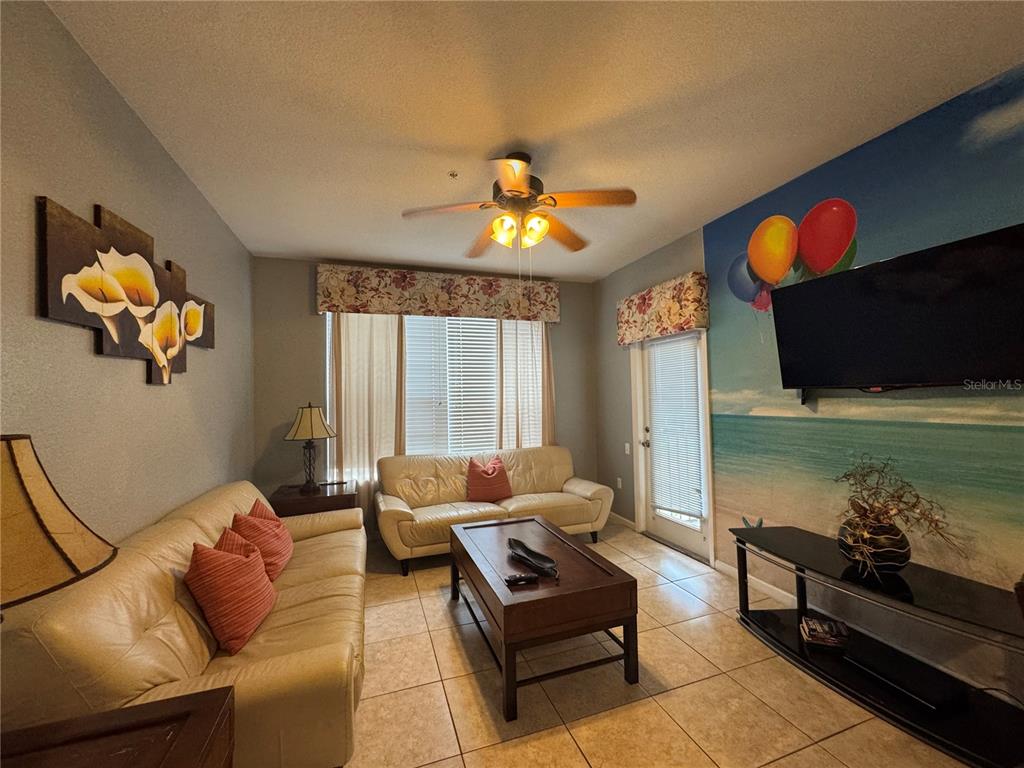 A living room features two beige leather sofas, a coffee table, and a beach-themed mural — 7664 COMROW STREET UNIT 204, KISSIMMEE, FL