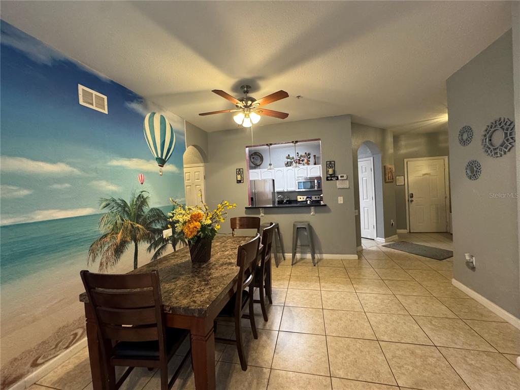 A dining area features a beach mural, tile flooring, and a pass-through to the kitchen — 7664 COMROW STREET UNIT 204, KISSIMMEE, FL
