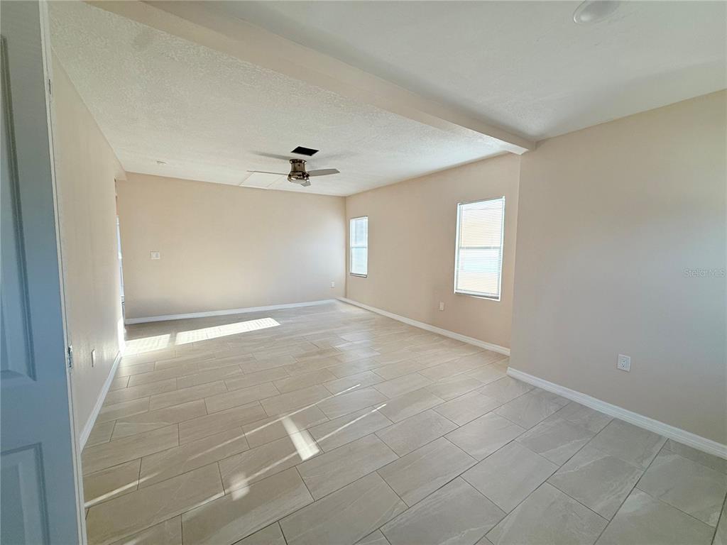 An empty room features light-colored tile flooring, beige walls, and a ceiling fan — 1015 23RD AVENUE W, BRADENTON, FL