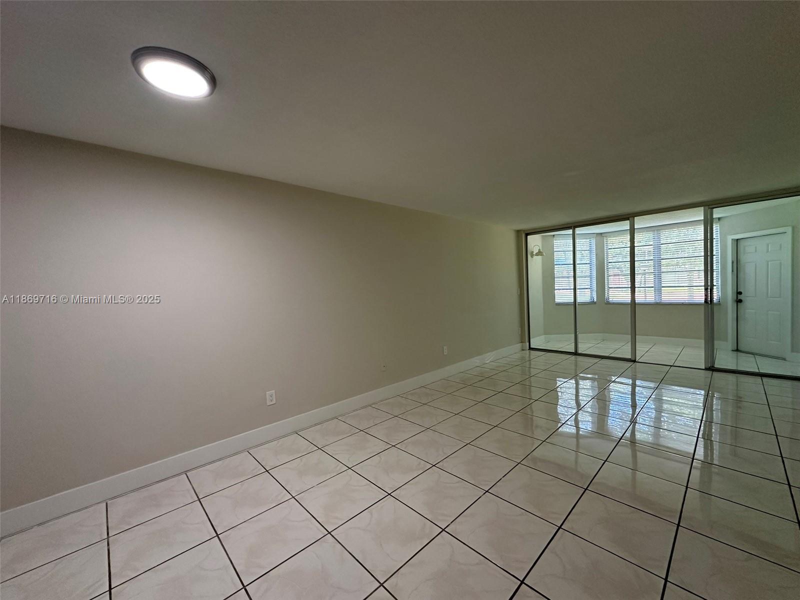An empty room features light-colored tile flooring, beige walls, and a sliding glass door — 1501 NE 191st St # C108, Miami FL 33179, MIAMI, FL
