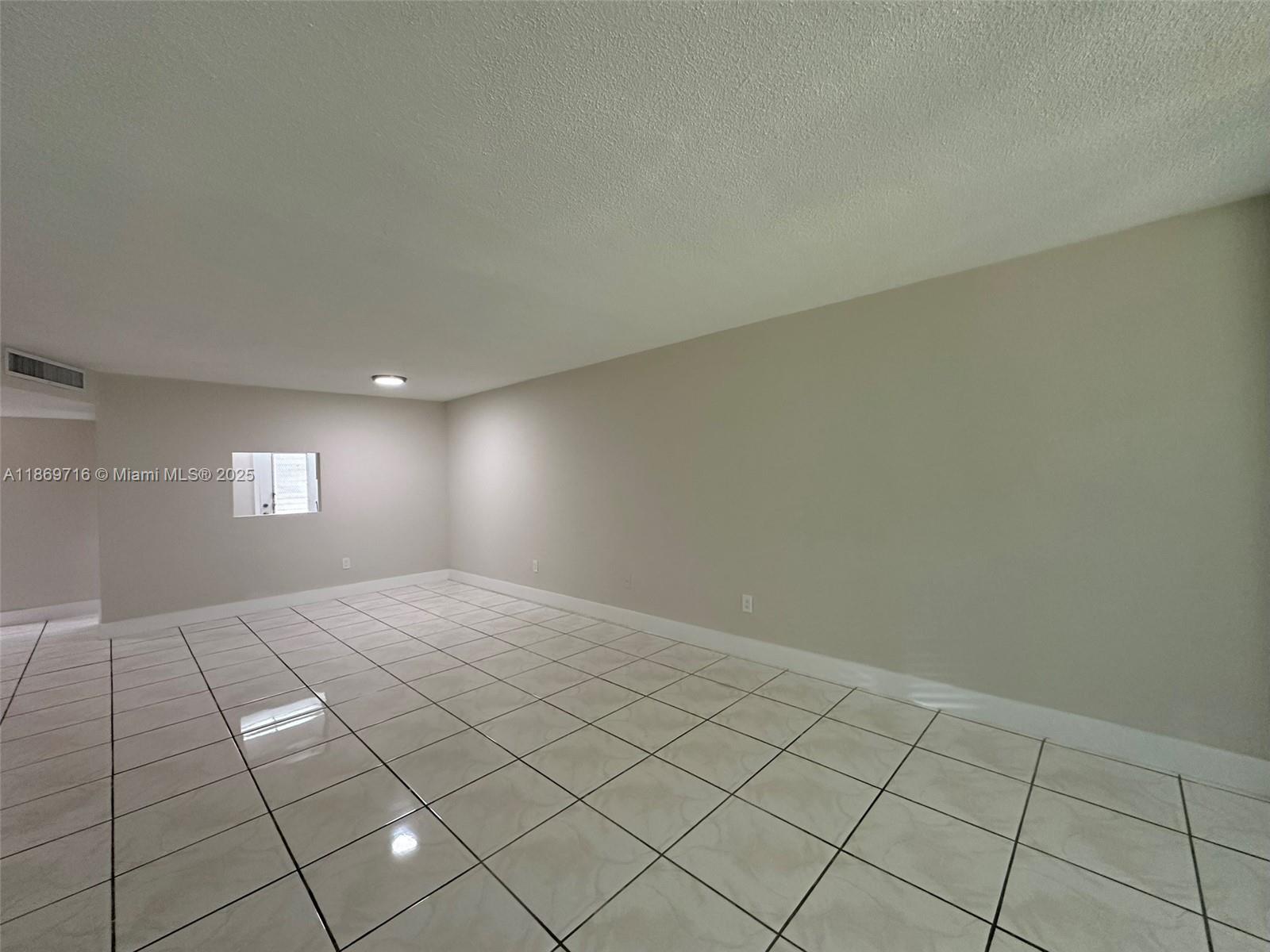 An empty room features light-colored tile flooring, beige walls, and a small square window — 1501 NE 191st St # C108, Miami FL 33179, MIAMI, FL
