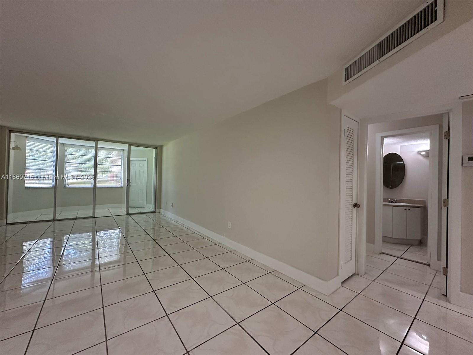 A living area with light-colored tile flooring leads to a glass-enclosed balcony and a bathroom — 1501 NE 191st St # C108, Miami FL 33179, MIAMI, FL