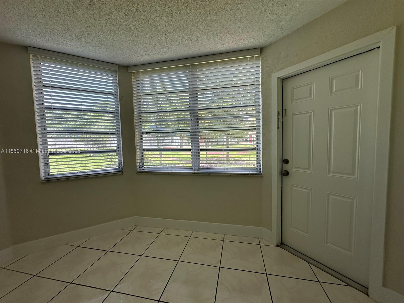 A room with white tile floors, two windows with blinds, and a white entry door — 1501 NE 191st St # C108, Miami FL 33179, MIAMI, FL