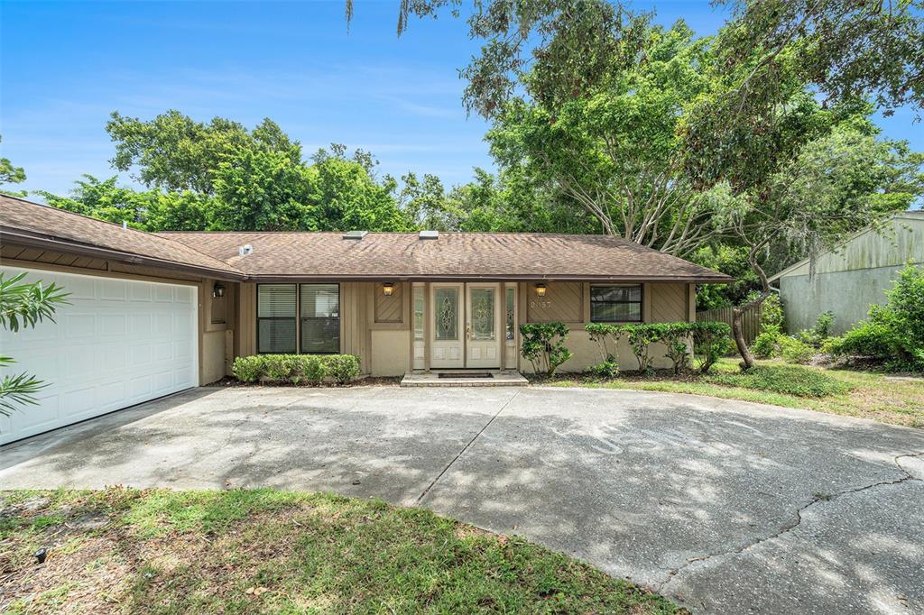 A single-story house with a brown shingled roof, beige siding, and a concrete driveway — 2057 BRENT PLACE, PALM HARBOR, FL