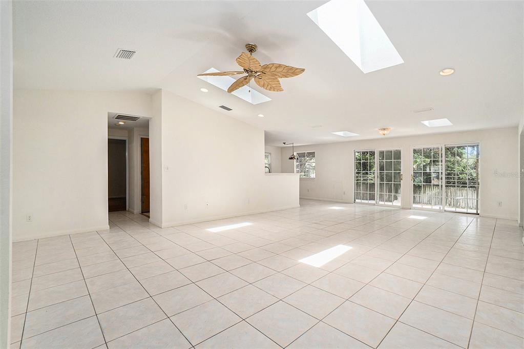 A bright, open-concept living area features white tile floors, a ceiling fan, and multiple skylights — 2057 BRENT PLACE, PALM HARBOR, FL