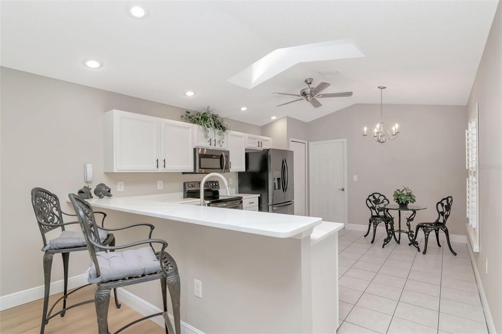 A kitchen with white cabinets, a breakfast bar, and an adjacent dining area with tile — 9500 GREEN NEEDLE DRIVE, NEW PORT RICHEY, FL