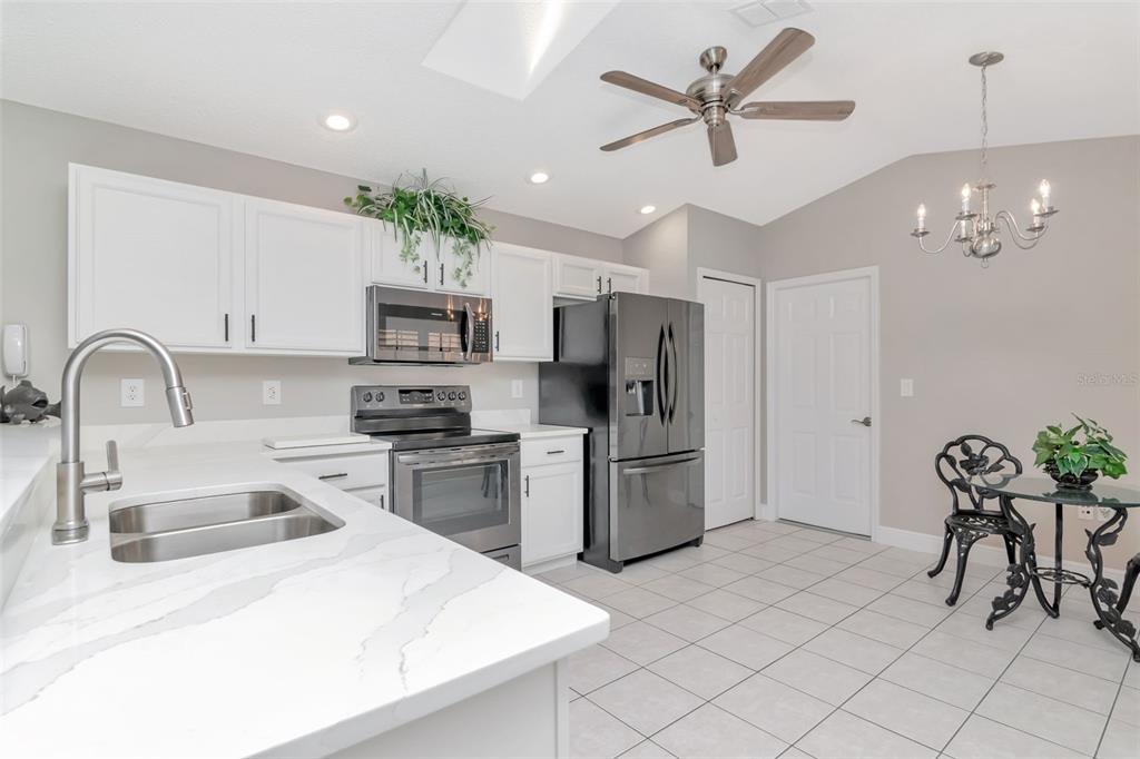 A kitchen features white cabinets, stainless steel appliances, a ceiling fan, and a dining area — 9500 GREEN NEEDLE DRIVE, NEW PORT RICHEY, FL