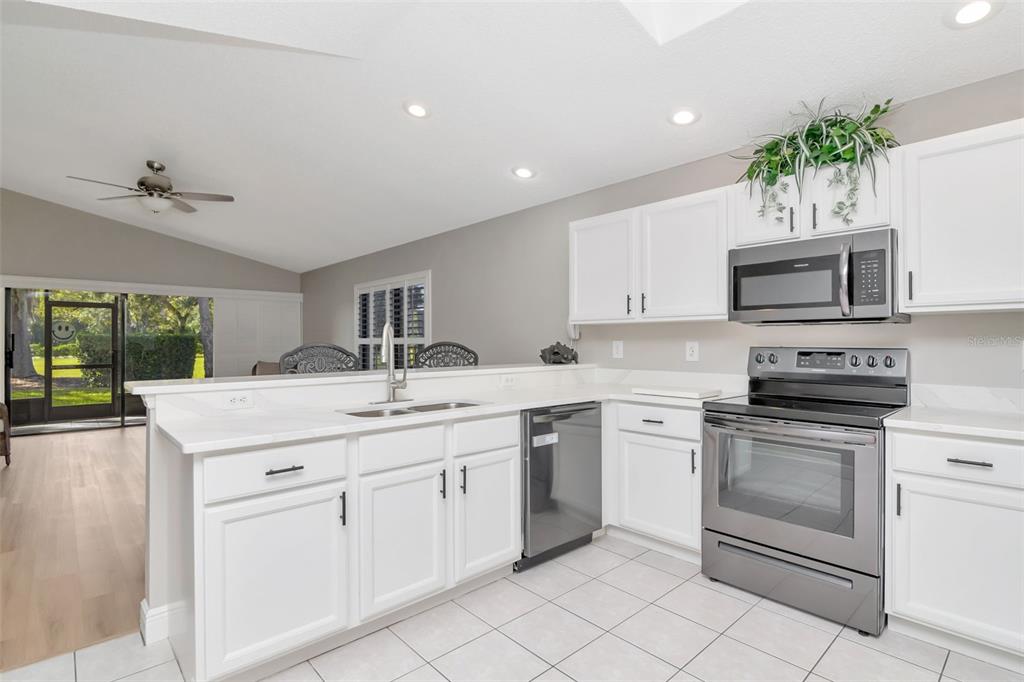 A kitchen with white cabinets, stainless steel appliances, and a peninsula overlooking a living area — 9500 GREEN NEEDLE DRIVE, NEW PORT RICHEY, FL