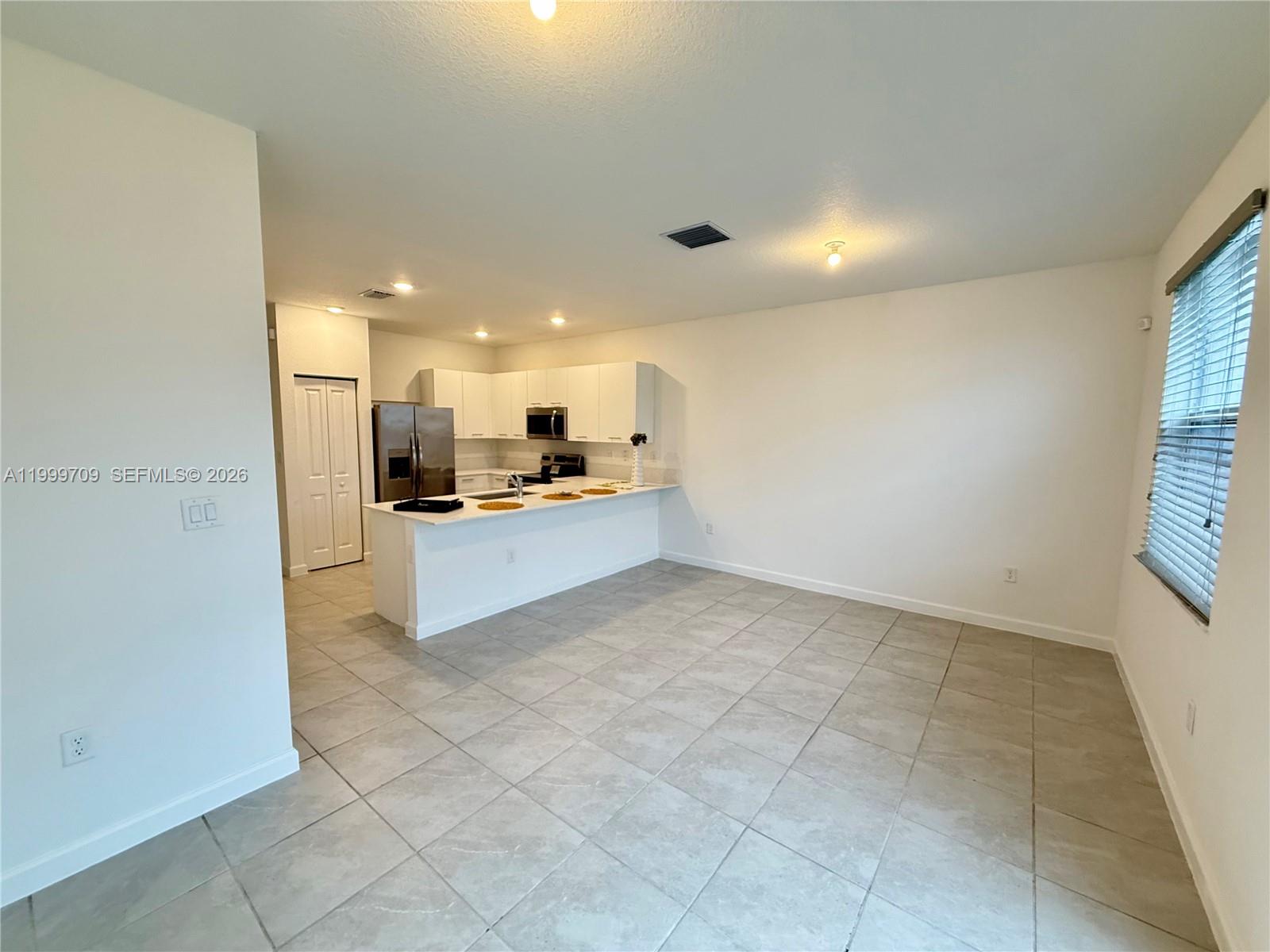 A kitchen with white cabinets and stainless steel appliances opens to a tiled living area — 12223 NW 23rd Pl, Miami FL 33167, MIAMI, FL