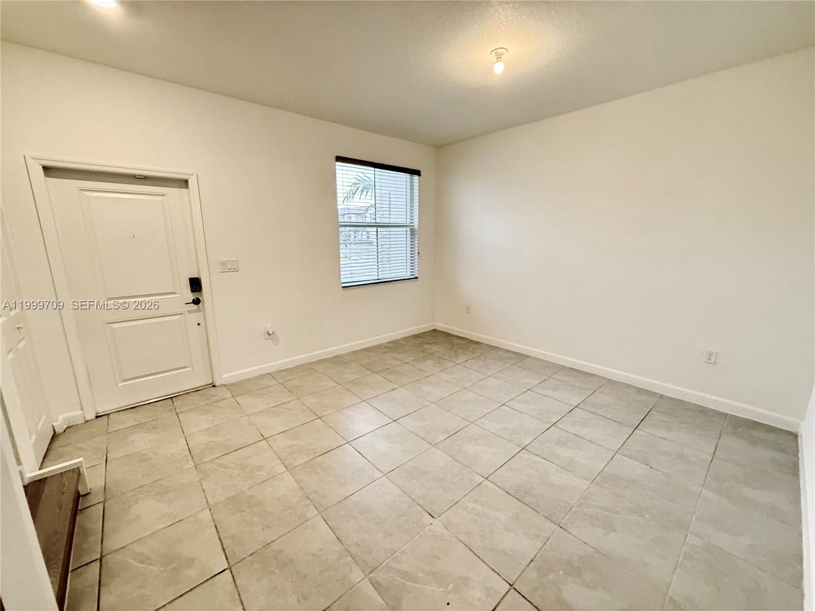 An empty room features white walls, light-colored tile flooring, a window, and a white door — 12223 NW 23rd Pl, Miami FL 33167, MIAMI, FL