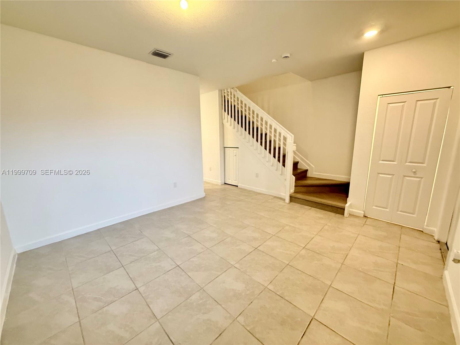 An empty room features light-colored tile flooring, white walls, and a staircase with wooden steps — 12223 NW 23rd Pl, Miami FL 33167, MIAMI, FL