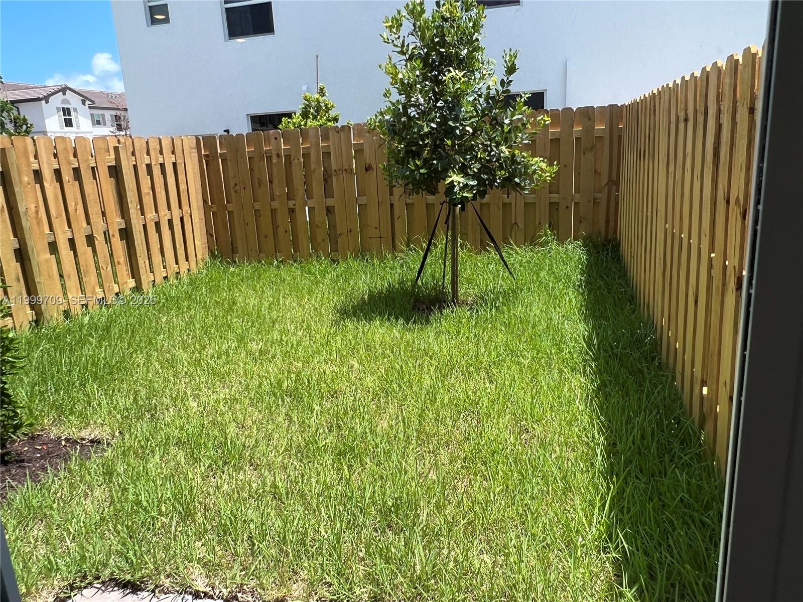 A small backyard features a green lawn, a young tree, and a wooden fence — 12223 NW 23rd Pl, Miami FL 33167, MIAMI, FL