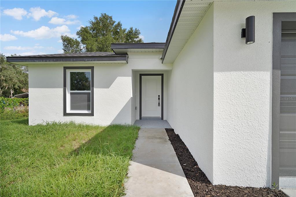 A concrete walkway leads to the white front door of a house with stucco siding — 13969 SW 45TH TERRACE, OCALA, FL