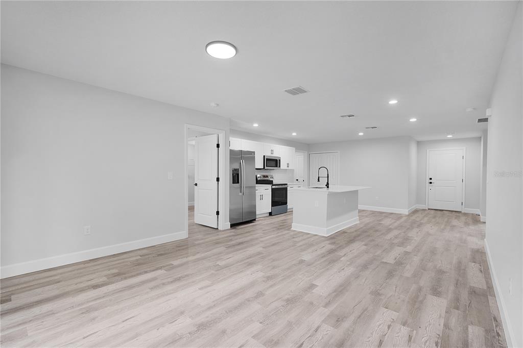 An open-concept kitchen features white cabinetry, stainless steel appliances, and light wood-look flooring — 13969 SW 45TH TERRACE, OCALA, FL