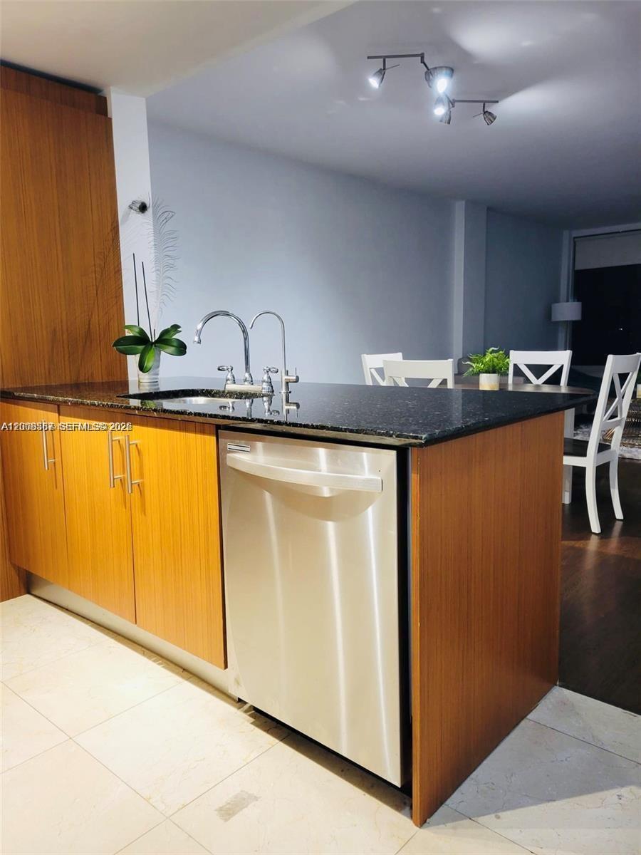 A kitchen island features a stainless steel dishwasher, a dark countertop, and wood-grain cabinets — 10275 Collins Ave # 327, Bal Harbour FL 33154, BAL HARBOUR, FL