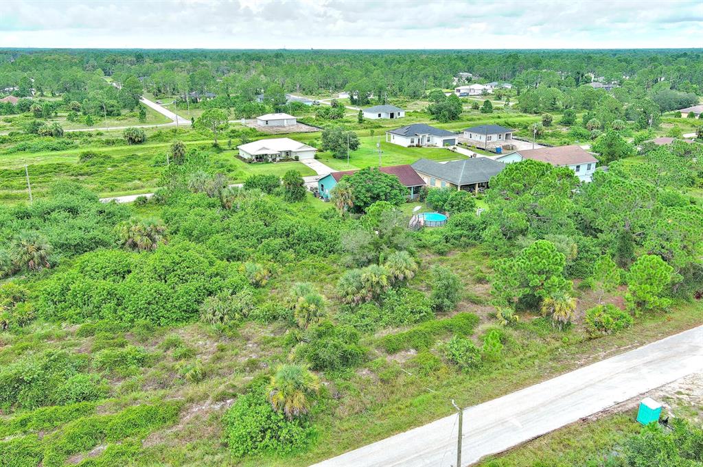 An aerial view shows a residential neighborhood with houses surrounded by dense, undeveloped vegetation — 928 NORFOLK AVENUE S, LEHIGH ACRES, FL