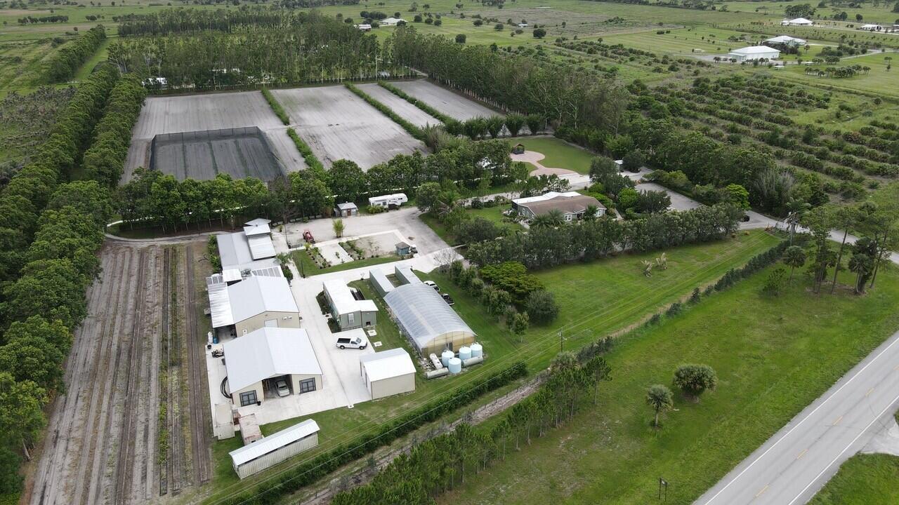 An aerial view shows a rural property with a house, outbuildings, greenhouse, and agricultural fields — 8006 SW Kanner Highway, FL 34956, FL